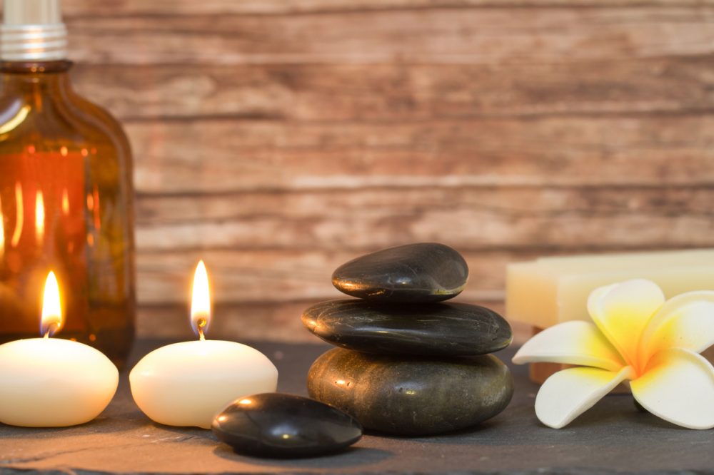 wellness and spa composition with candles, stacked massage stones and oil